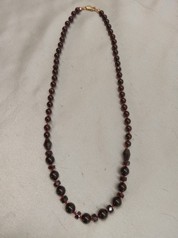 picture of necklace made of both round and shaped and faceted garnet beads, approximately 19 inches long